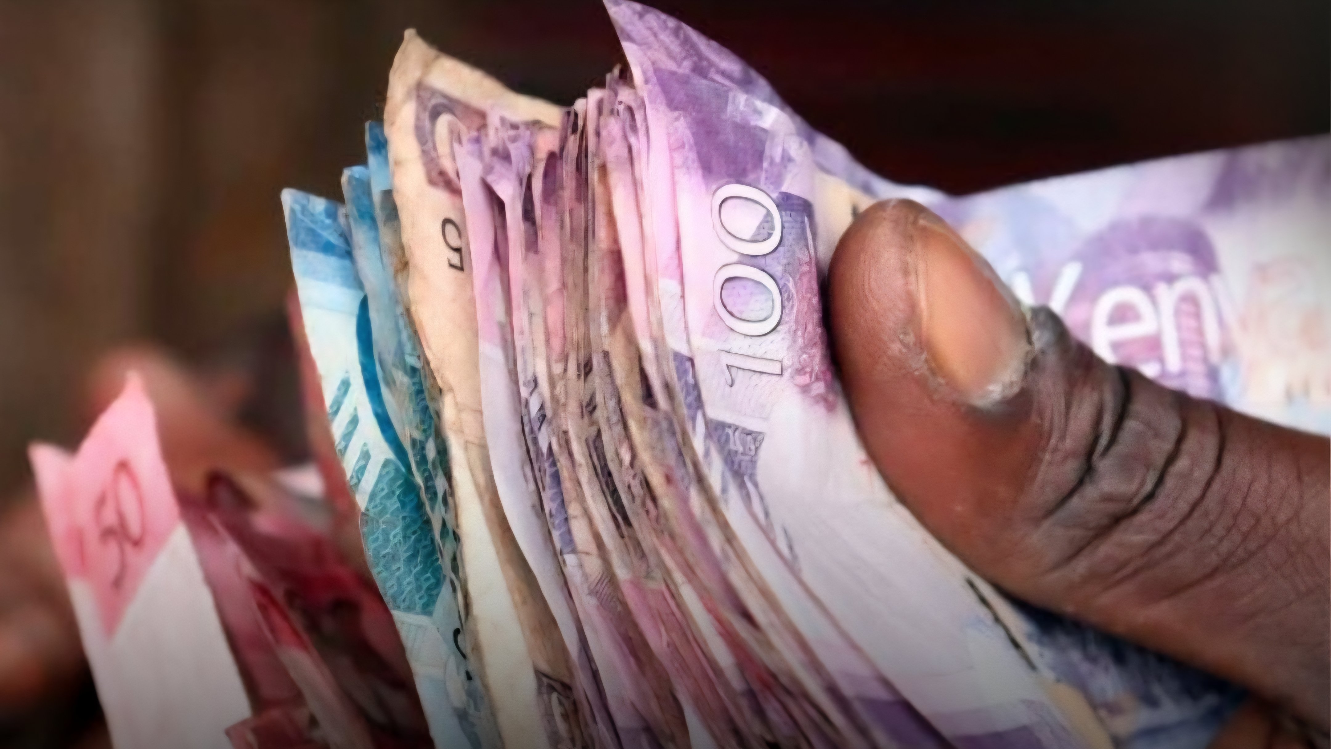 A close-up view of a person holding several Kenyan Shilling banknotes of different denominations including five hundred and one thousand shilling notes.