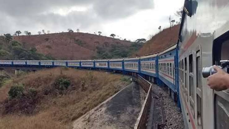 A passenger train traveling along a curved track through a rural, hilly landscape in East Africa.