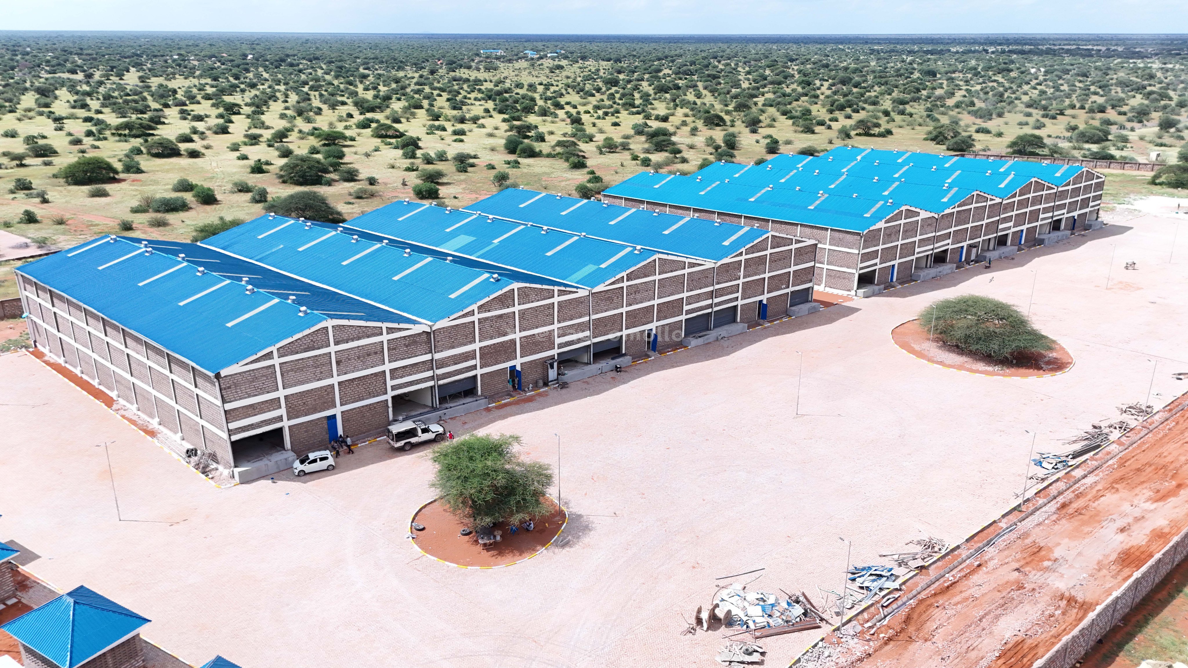 Aerial view of the large blue-roofed industrial sheds and concrete yards at the Wajir County Aggregation and Industrial Park construction site.