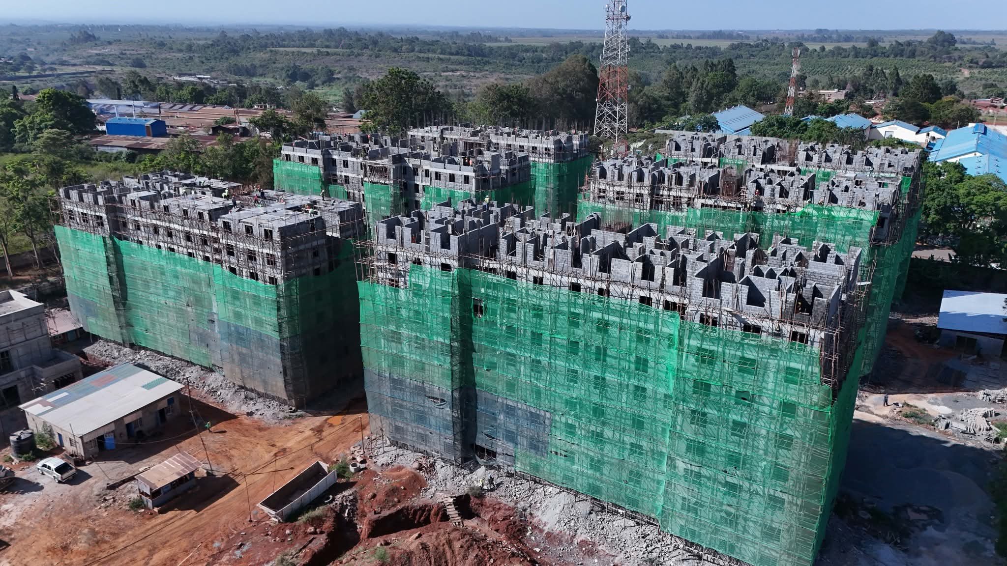 A wide angle view of a large residential construction site in Kenya showing multiple apartment blocks under development with scaffolding and cranes visible.