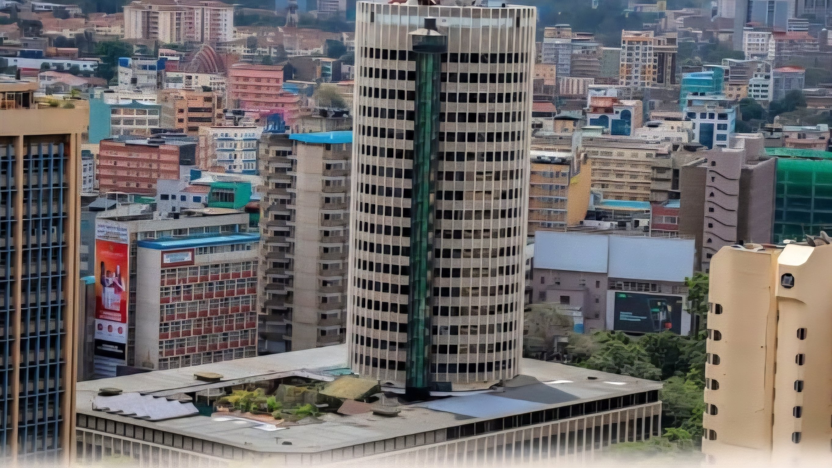 Exterior wide shot of the Hilton Hotel's cylindrical tower in Nairobi CBD, showing the glass-paneled elevator shaft and surrounding city buildings under a clear sky.