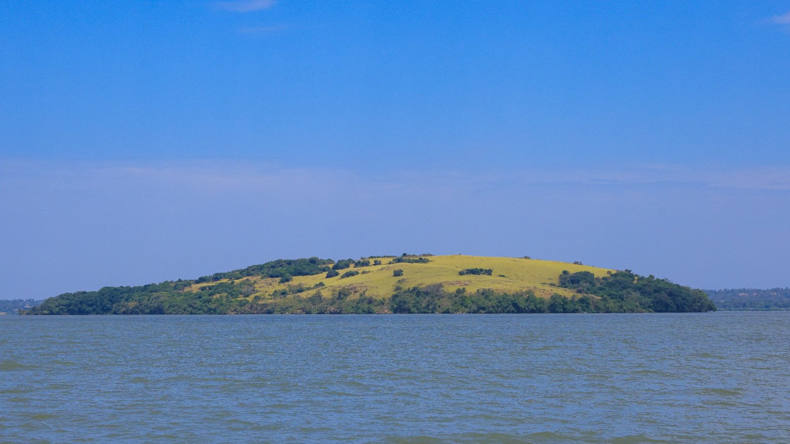 Panoramic view of the rolling green and red hills of Ndere Island National Park set against the waters of Lake Victoria in Kisumu, Kenya.