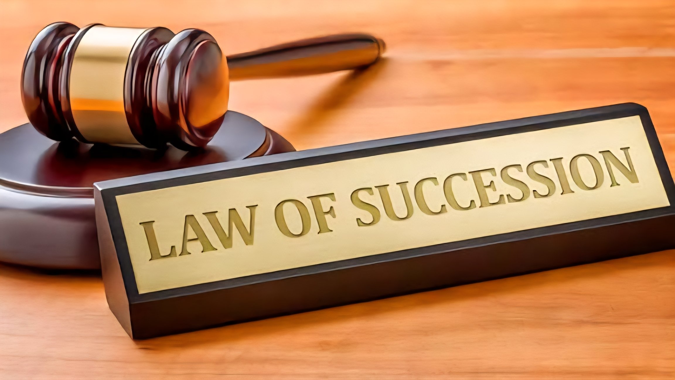 A wooden gavel rests on a desk next to a green block inscribed with the words Law of Succession.